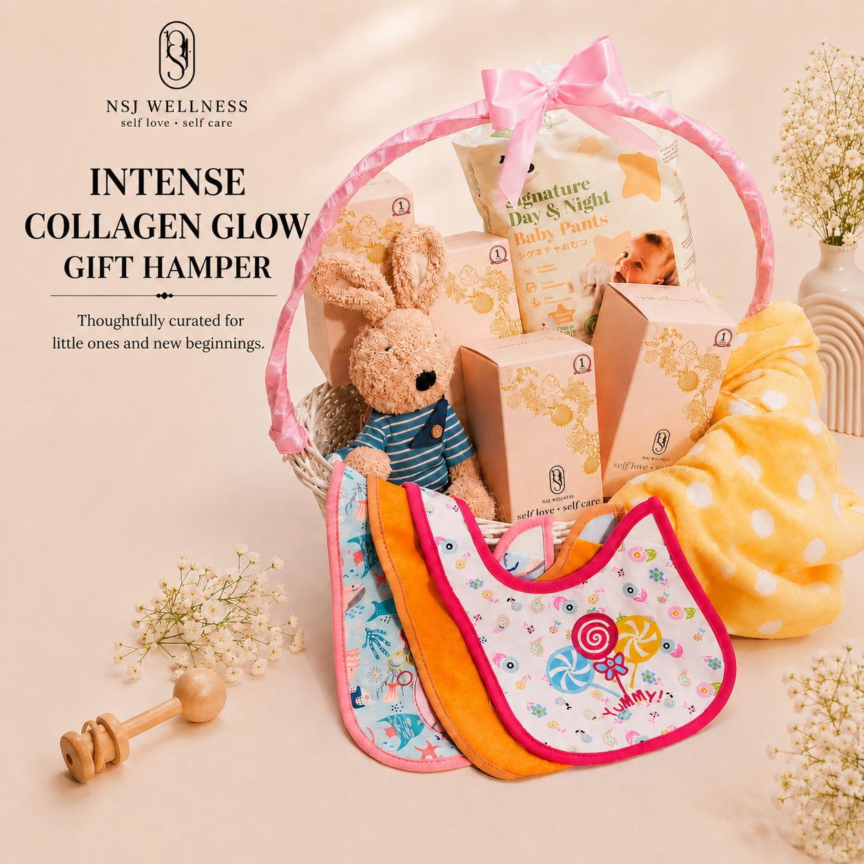Intense Collagen Glow Baby Hamper with sachet boxes, baby pants, bibs, a yellow blanket and a knitted bunny in a pink basket