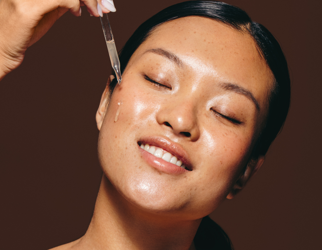 Woman applying a serum with a dropper to her glowing skin, the anti-ageing collection banner